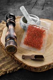 Wooden cross section with saffron in plastic package and stone mortar and mill