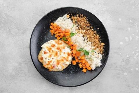 Chopped pork cutlet baked with ham and cheese served with carrot and rice on a plate