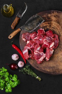 Overhead view of chopping fresh beef meat for goulash or stew on wooden chopping stump