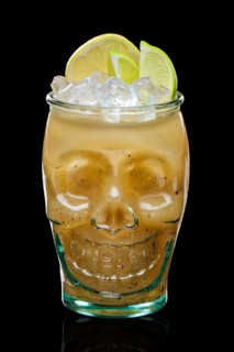 Halloween feijoa cocktail with slices of lime and lemon in skull glass isolated on black