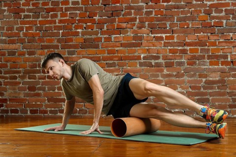 Young male cyclist athlete training and doing workout with barrel on gym mat. Fitness workout