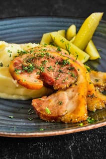 Close up view of baked bacon with mashed potato and pickle cucumber