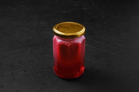 Whole closed jar of cherry jam on black background