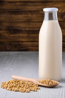 Bottle of soy milk with soybeans on white table over dark wooden background