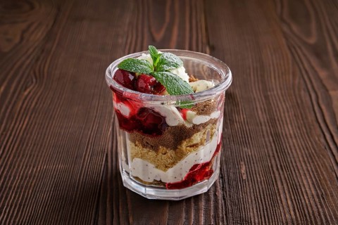 Delicious tiramisu dessert with cherry in rustic pot on dark wooden background