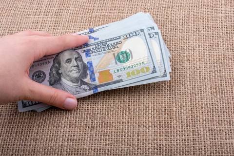 Hand holding banknote bundle of US dollar on a linen canvas background