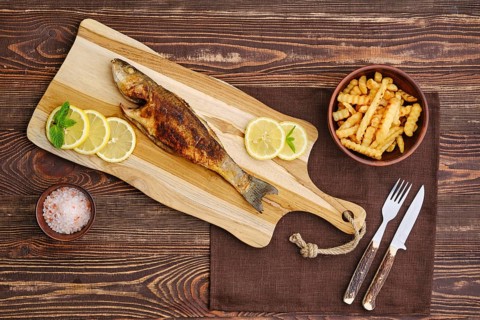 Top view of fried sea bass with fried potato on wooden cutting board