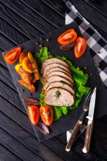 Sliced baked ham with fresh tomatoes on a stone plate in a rustic style
