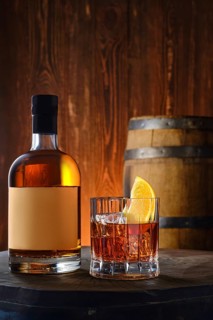 Bottle and glass with blended malt scotch whisky with a barrel on background