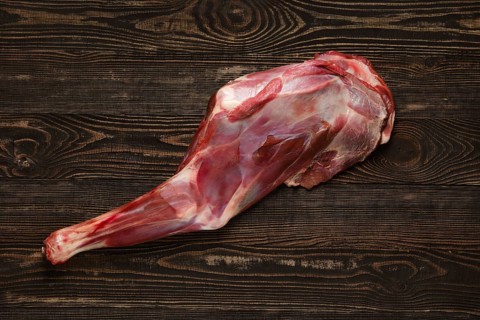 Overhead view of raw doe leg over wooden background