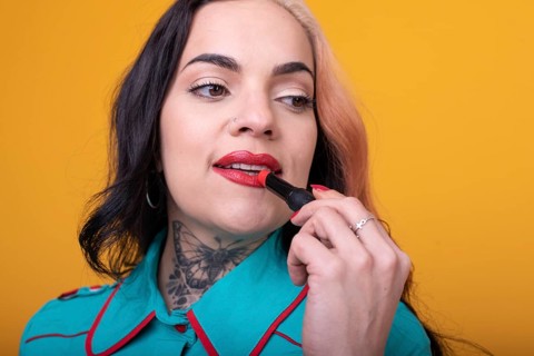 Beautiful caucasian woman applying a bright red color lipstick on her lips over yellow background