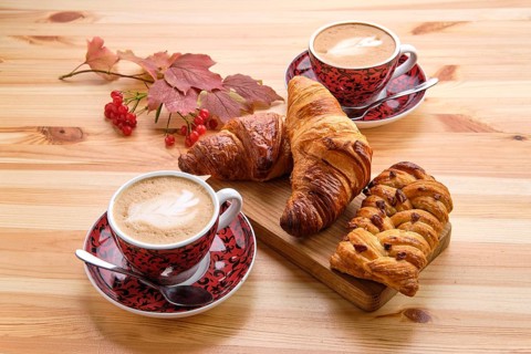 Puff pastry raisin bun and crispy croissant on wooden table with coffee