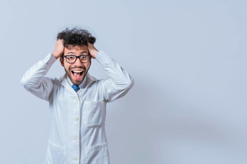 A mad scientist pulling his hair out on isolated background. Mad scientist grabbing his hair with a mad face isolated. A doctor with a crazy face looking at the camera
