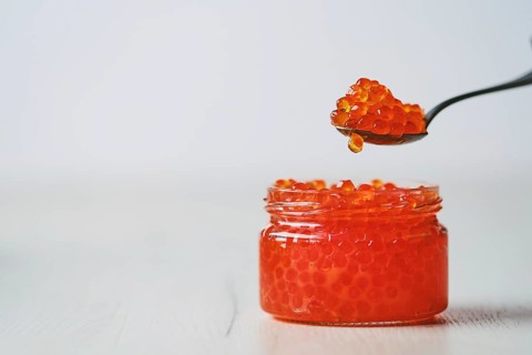 Photo with shallow depth of field of open jar with red caviar and a spoon above it