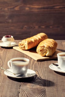 Rolled buns and coffee on wooden table in morning sunlight. Photo with shallow depth of field