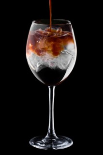 Pouring spresso in cocktail with tonic in wine glass isolated on black background