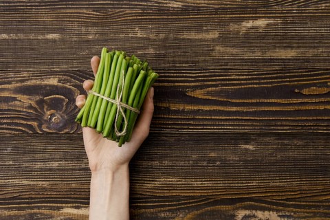 Overhead view of fresh green beans in hand over wooden background