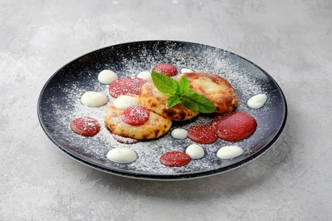 Sweet curd patties with sour cream and strawberry jam on a plate