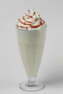 Melon and caramel milkshake summer cocktail in tall facetted glass on gray background