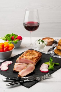 Sliced grilled pork fillet with fresh tomatoes and raddish served with glass of red wine
