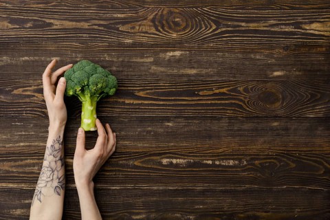 Overhead view of fresh broccoli in hands over wooden background