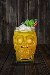 Halloween cocktail in goblet skull on wooden shelf. Jolly Roger drink in glass cup in the shape of skull