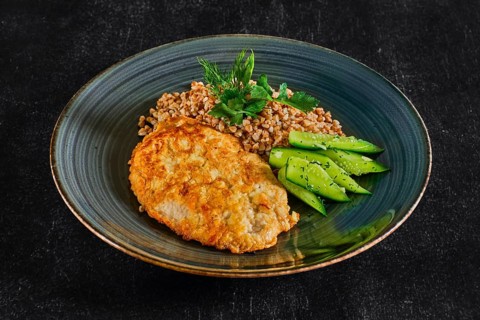 Top view of chicken fillet fried in batter with buckwheat porridge and pickled cucumber