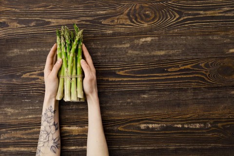 Overhead view of fresh asparagus in hand over wooden background