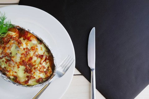 Top view of meat baked in foil with vegetables and cheese on wooden table