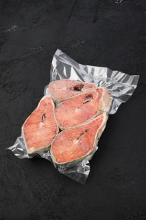 Overhead view of raw salmon steak in vacuum packaging on dark background