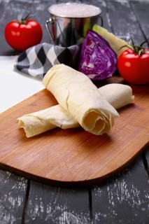 Rolled pita with fresh vegetables on wooden board with a napkin on a table