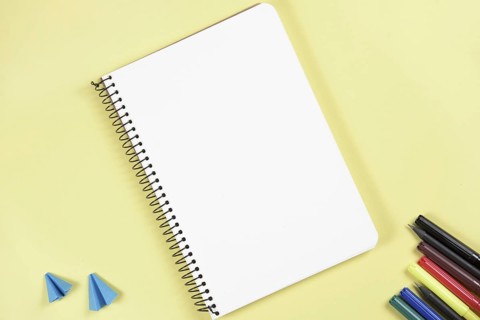 Folded craft paper felt tip pen near blank spiral notepad yellow background