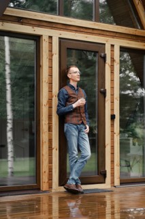 Pensive middle age man stands on the terrace of a wooden bungalow and drinks bourbon