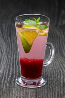 Tall transparent glass with raspberry and citrus tea on dark wooden table