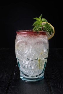 Variation of gin and tonic cocktail with cherry syrup in skull cup on dark wooden background