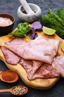 Raw fresh unpeeled squid on wooden cutting board with spice and herbs