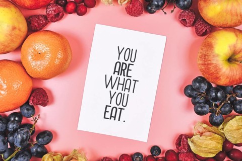 Healthy eating concept with You are what you eat card on pink background surrounded by fruits like apples