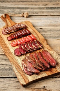 Slices of smoked dried beef and pork meat on wooden cutting board
