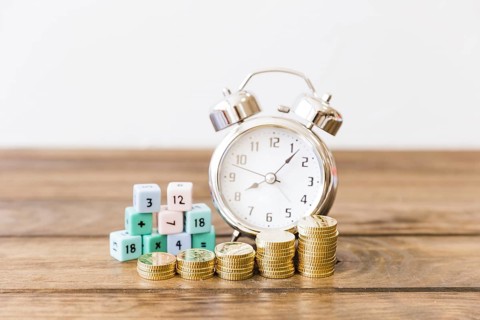 Close up stacked coins front alarm clock math blocks wooden desk