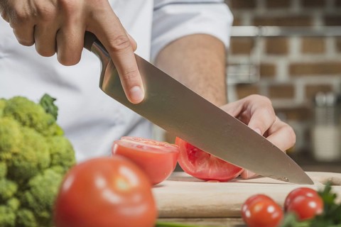 Chef s male hand cutting tomato with sharp knife board
