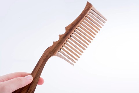 Hand holding a wooden hair comb on a white background