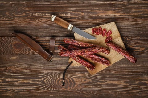 Overhead view of dried jerked deer and pork sausage on wooden background