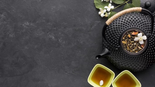 Dried tea herb ingredient with black teapot slate stone background