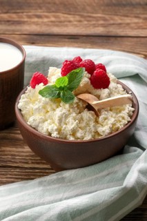 Fresh cottage cheese with raspberries and wooden spoon in clayware on wooden table