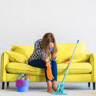 Frustrated young woman sitting sofa with cleaning equipments