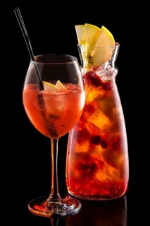 Cold sangria in pitcher and wine glass with ice cubes isolated on black background