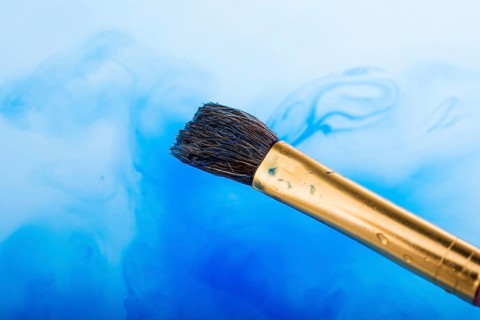 Watercolor paint dissolving in water as painting brush touches water