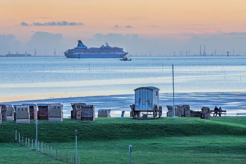 Grassy beach with beach chairs and cruise ship Artania on the Weser at dusk