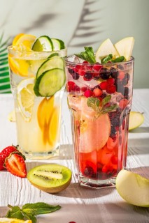 Variations of lemonades with different fruits and syrups on white wooden table under morning sun