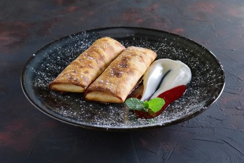 Sweet pancakes stuffed with curd and decorated with sour cream and strawberry jam